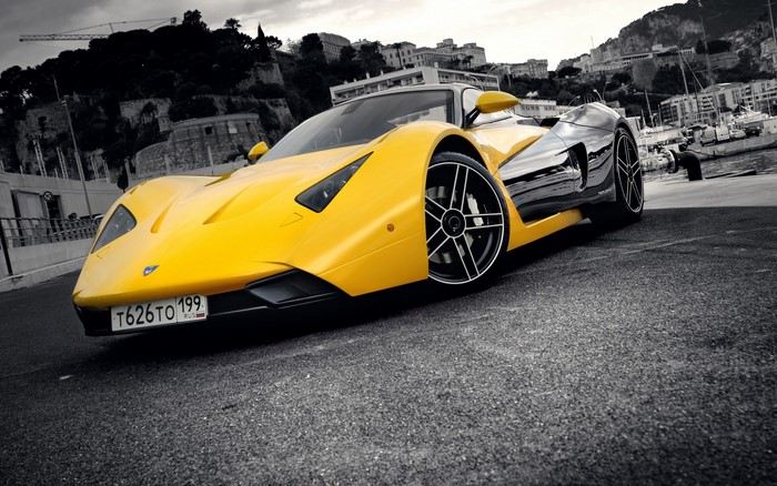 Yellow Marussia B2 sports car parked by a harbor
