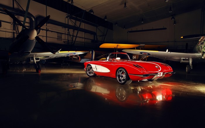 Red 1950s Corvette in hangar with airplanes