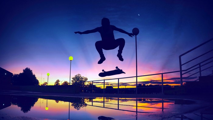 Silhouette of a skateboarder jumping at sunset with reflections