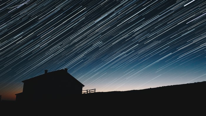 Star trails over a silhouetted house and hill