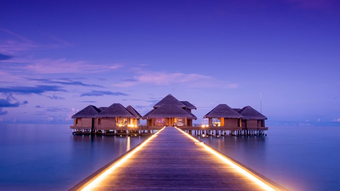 Overwater bungalows at twilight with illuminated walkway