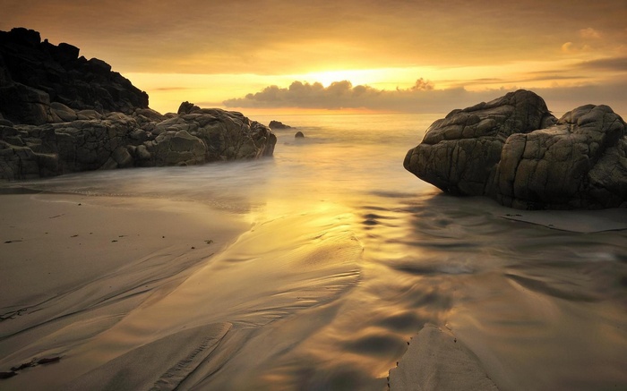 Golden sunset over a rocky beach with smooth waves