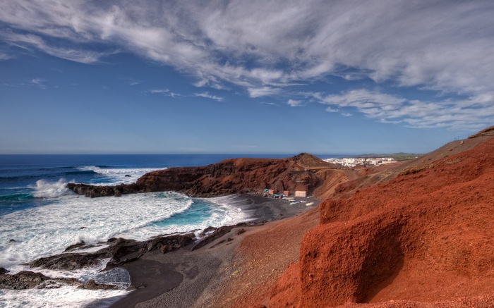 Red volcanic cliffs and black sand beach with ocean waves