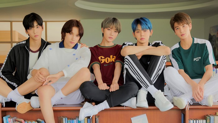 Five young men sitting on a bookshelf