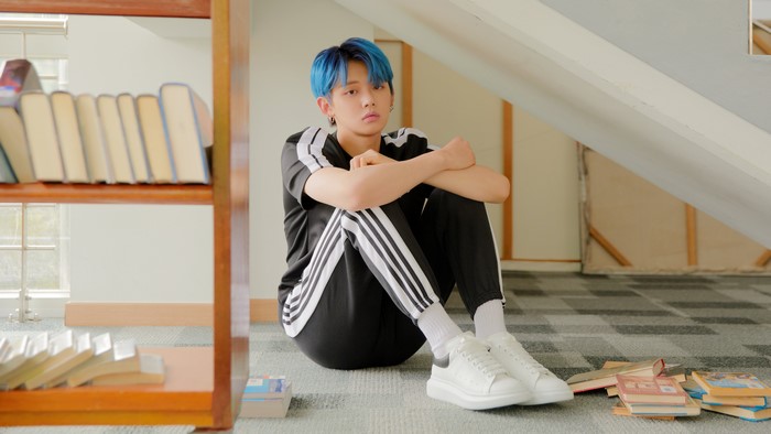 A young man with blue hair sitting on the floor