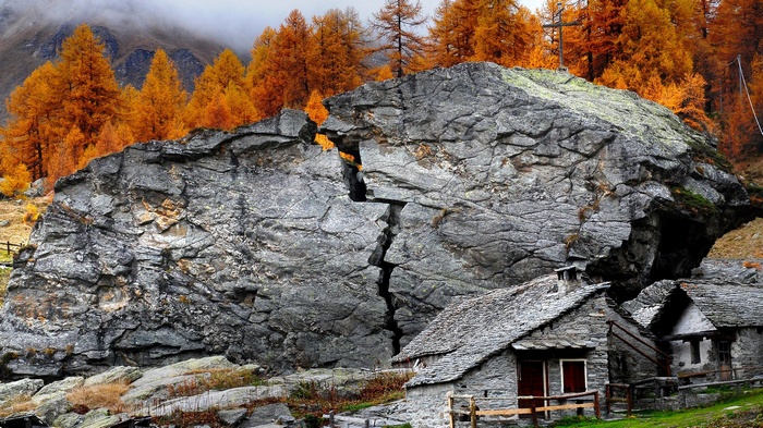 Stone houses nestled below a large cracked boulder and autumn trees