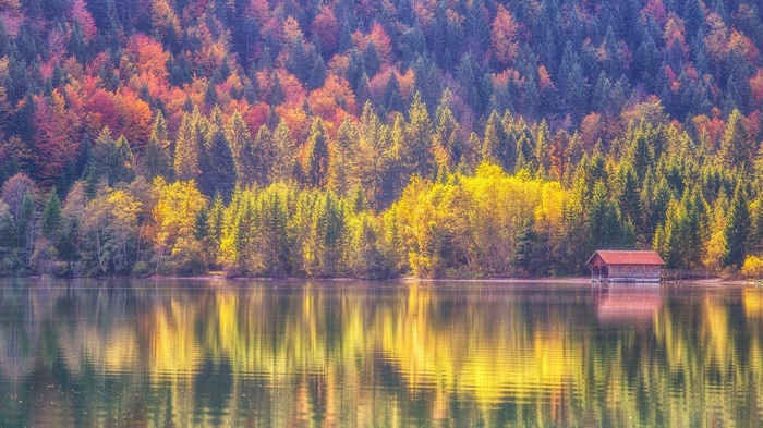 Autumn forest reflected in a lake with a boathouse