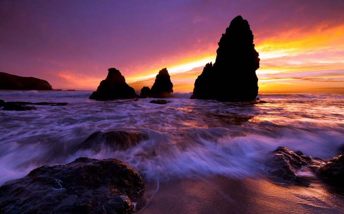 Ocean waves crash against rocky sea stacks at sunset