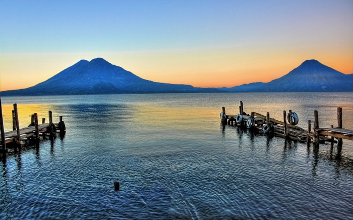 Two wooden docks on a lake with volcanoes at sunset