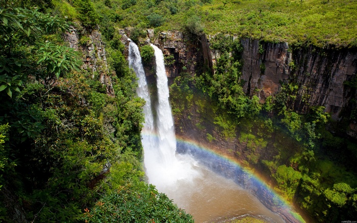 Waterfall with a rainbow in a lush green canyon