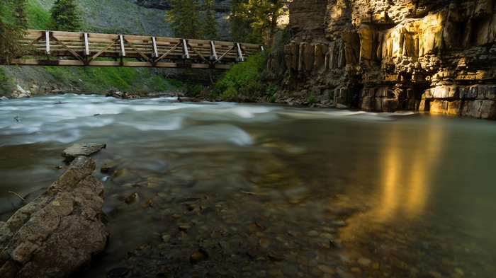 Wooden bridge over a river with rocky cliffs