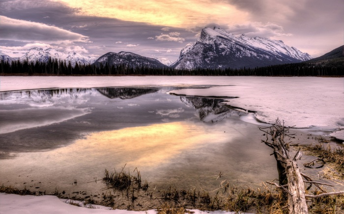 Frozen lake reflecting snow-capped mountains and cloudy sky