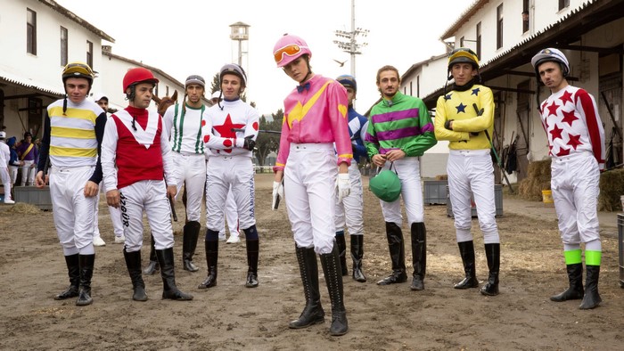 Group of jockeys in colorful racing silks standing outside stables