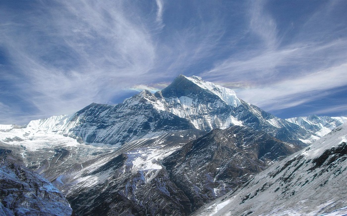Snow-covered mountain range under a cloudy blue sky