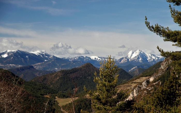 Snow-capped mountains and forested hills under a cloudy sky