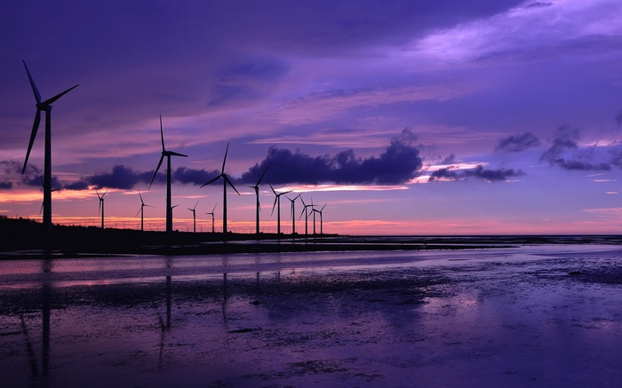 Wind turbines silhouetted against a purple sunset over water