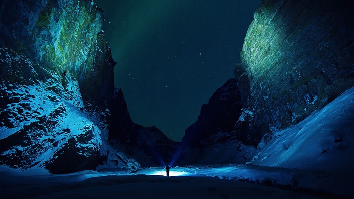 Man with flashlight in snowy mountains under starry sky