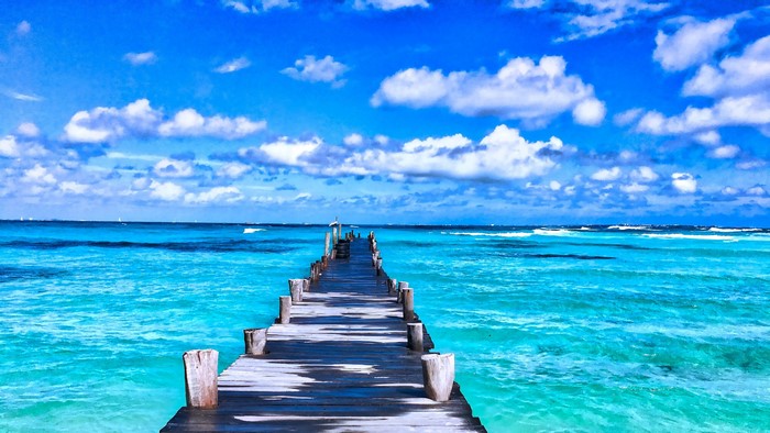 Wooden pier extending into a turquoise ocean under a blue sky with clouds, 4K