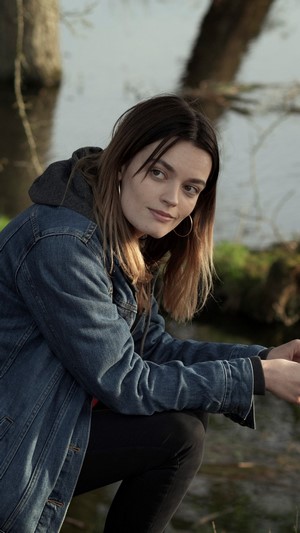 Emma Mackey crouching by a body of water