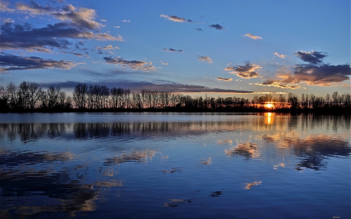 Sunset over a calm lake with trees and clouds reflected