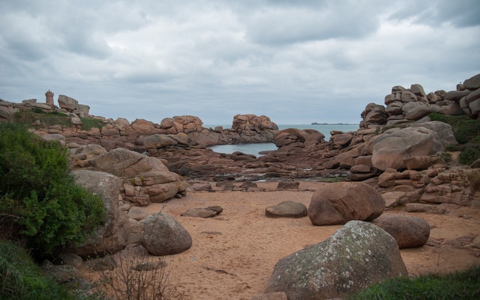 Pink granite boulders on a sandy beach with a lighthouse
