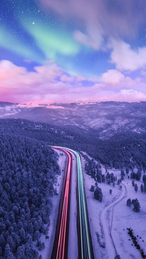 Aurora Borealis Over Snowy Mountains and Highway Light Trails