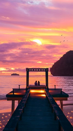 Couple on a pier watching a sunset over the ocean
