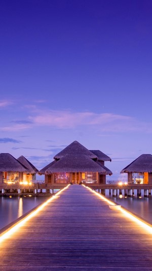 Overwater bungalows at sunset with illuminated walkway