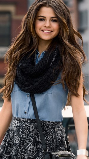 Selena Gomez smiling in a denim shirt and skull skirt