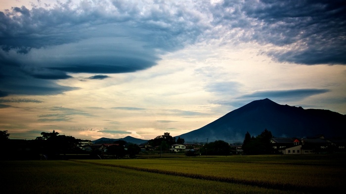 Mountain and field under cloudy sky