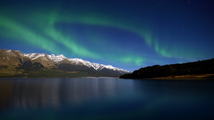 Aurora Borealis over snow-capped mountains and lake