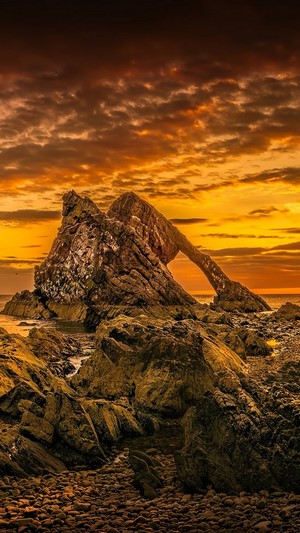Rock formation arching over the sea at sunset