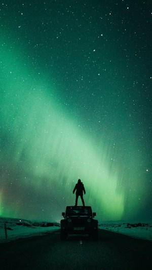 Person standing on car under Aurora Borealis