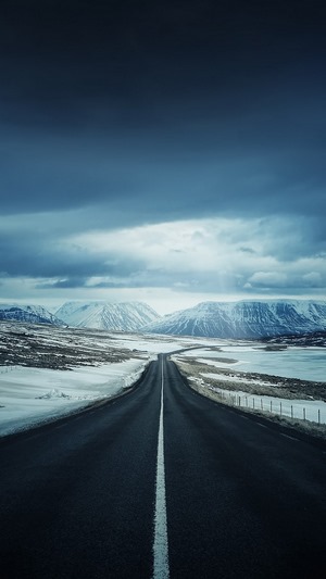 Road through snowy mountains under cloudy sky