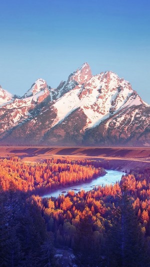 Snow-capped mountains over a colorful forest and river