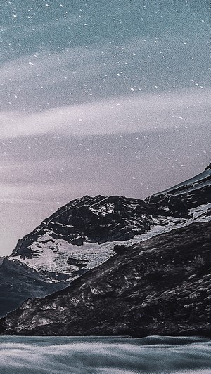 Snowy mountains overlooking a body of water under a starry sky