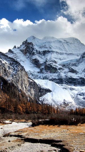Snow-capped mountain range with clouds and trees
