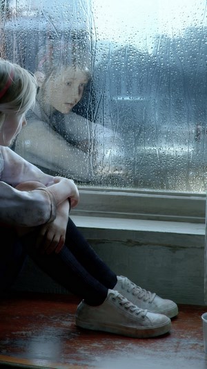 Girl looking out a rain-covered window