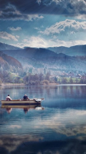Two people fishing in a boat on a lake with mountains in the background
