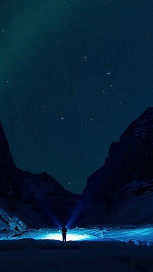 Person with flashlight under starry sky and aurora