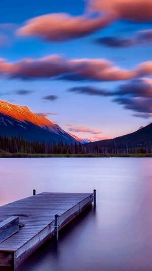 Wooden dock on a calm lake with mountains at sunset