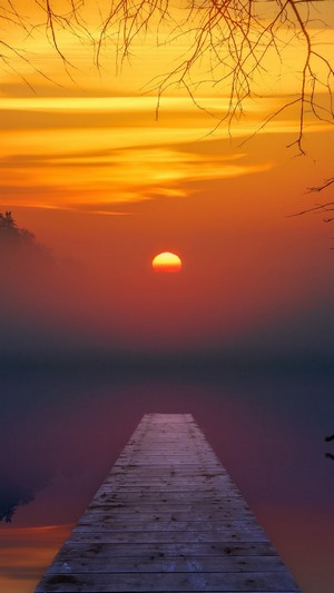 Sunset over a misty lake with a wooden pier
