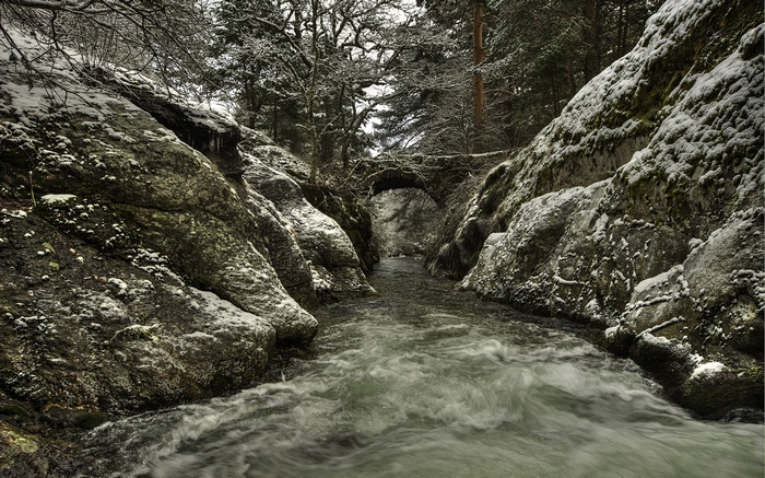 Snowy gorge with a river and an ancient stone bridge