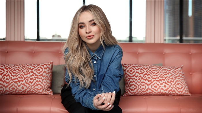 Sabrina Carpenter in a denim shirt on a pink couch