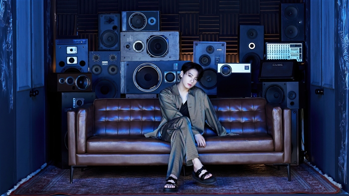 Jungkook from BTS sitting on a couch with speakers