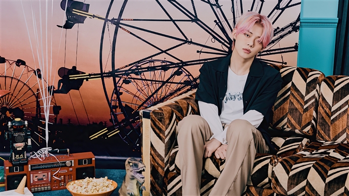 Yeonjun from TXT sitting on a couch with a carnival backdrop