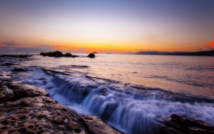 Ocean waves crashing on rocky shore at sunset