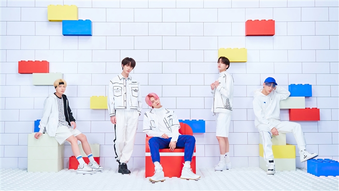 Tomorrow X Together members posing against a brick wall with colorful blocks