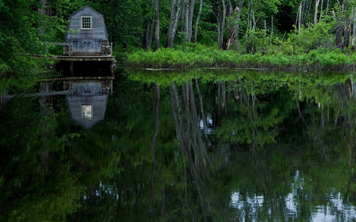 Wooden boathouse reflected in a calm lake surrounded by trees