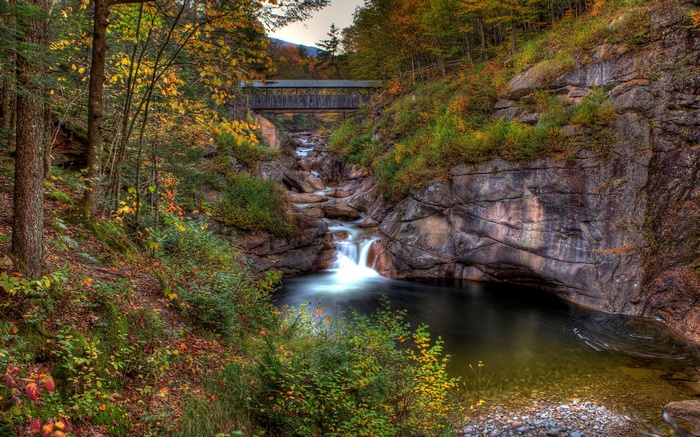Covered bridge over a waterfall in autumn forest